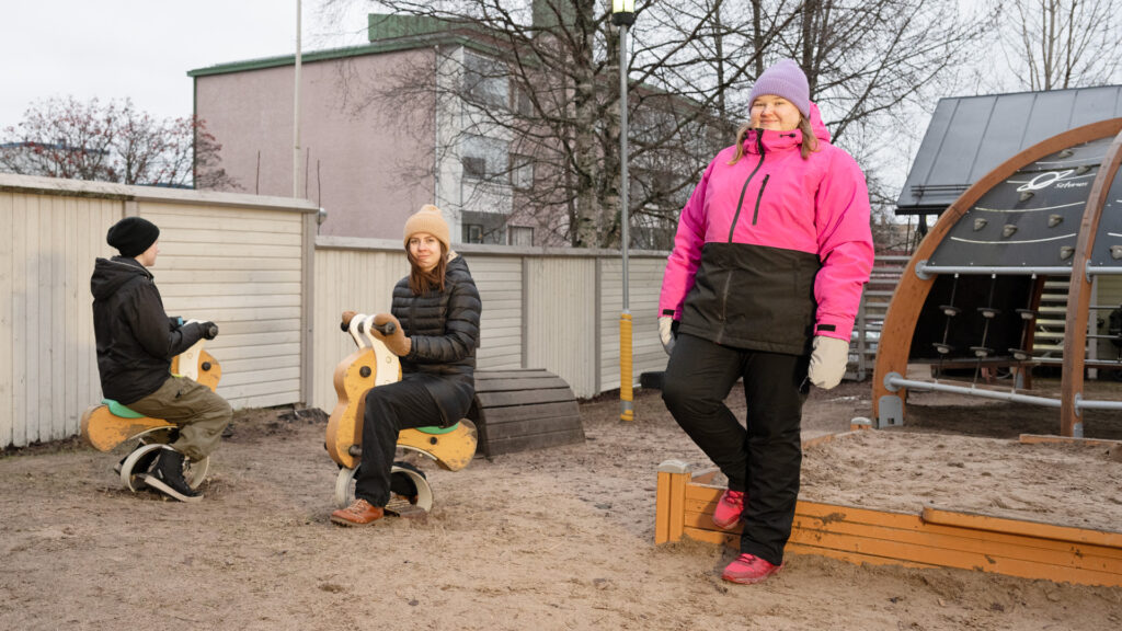 Kaksi opiskelijaa istuu keinuhevosten selässä ja yksi seisoo vieressä ja hymyilee. 